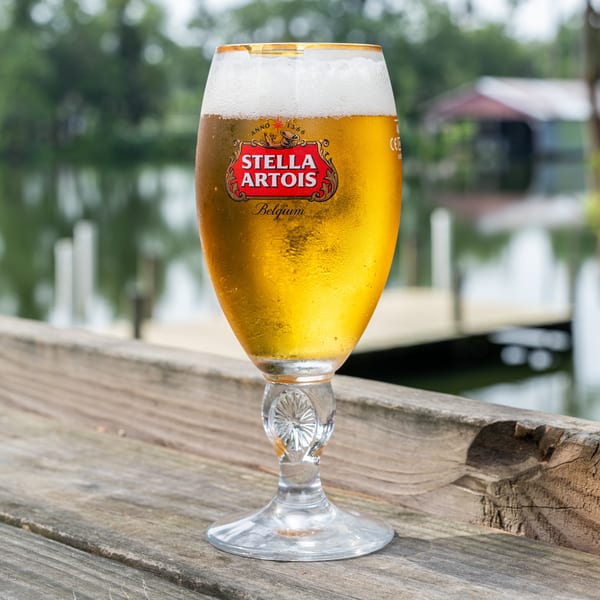 Cold Stella Artois beer in a branded glass on a wooden deck overlooking a lake.