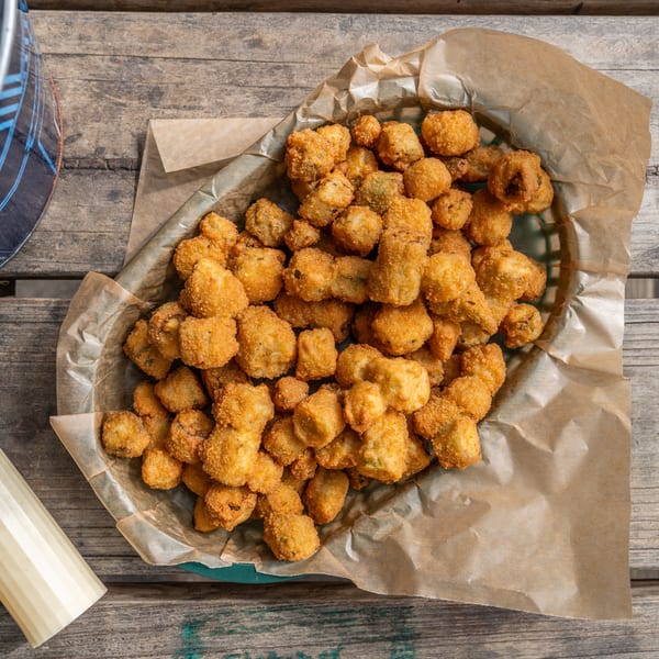 A basket of crispy golden-brown fried okra sits on a rustic wooden table.