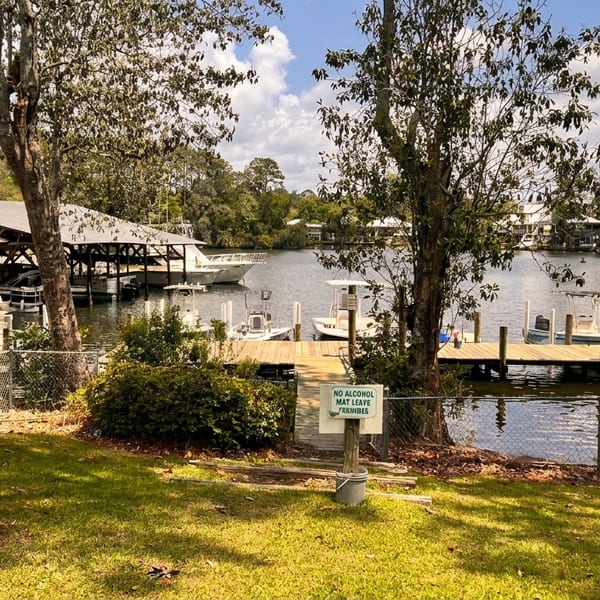 Restaurant patio overlooking a lake with boats docked at covered slips and a wooden pier.