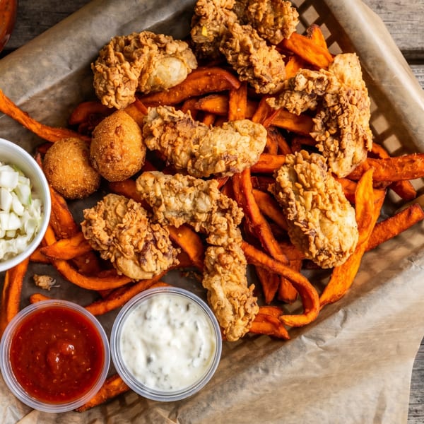 Fried chicken and sweet potato fries in a basket with coleslaw, red sauce, and white dipping sauce.