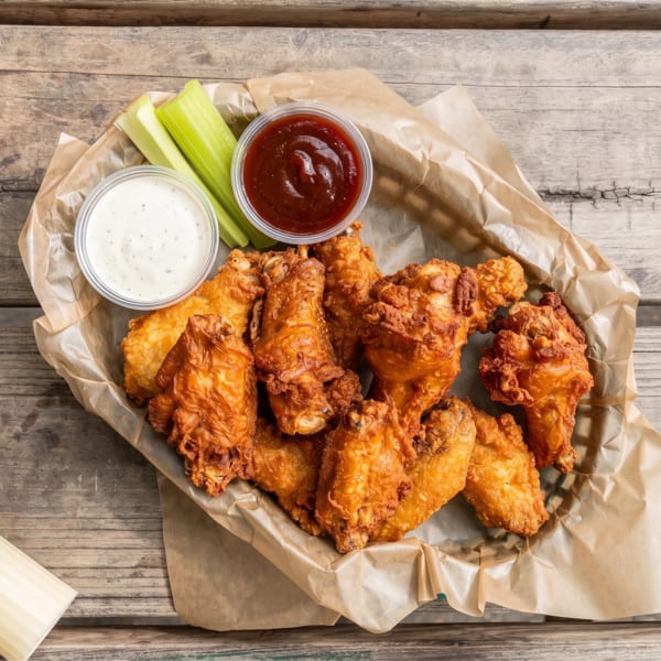 Crispy fried chicken wings with celery sticks, ranch, and barbecue sauce on a rustic wooden table.